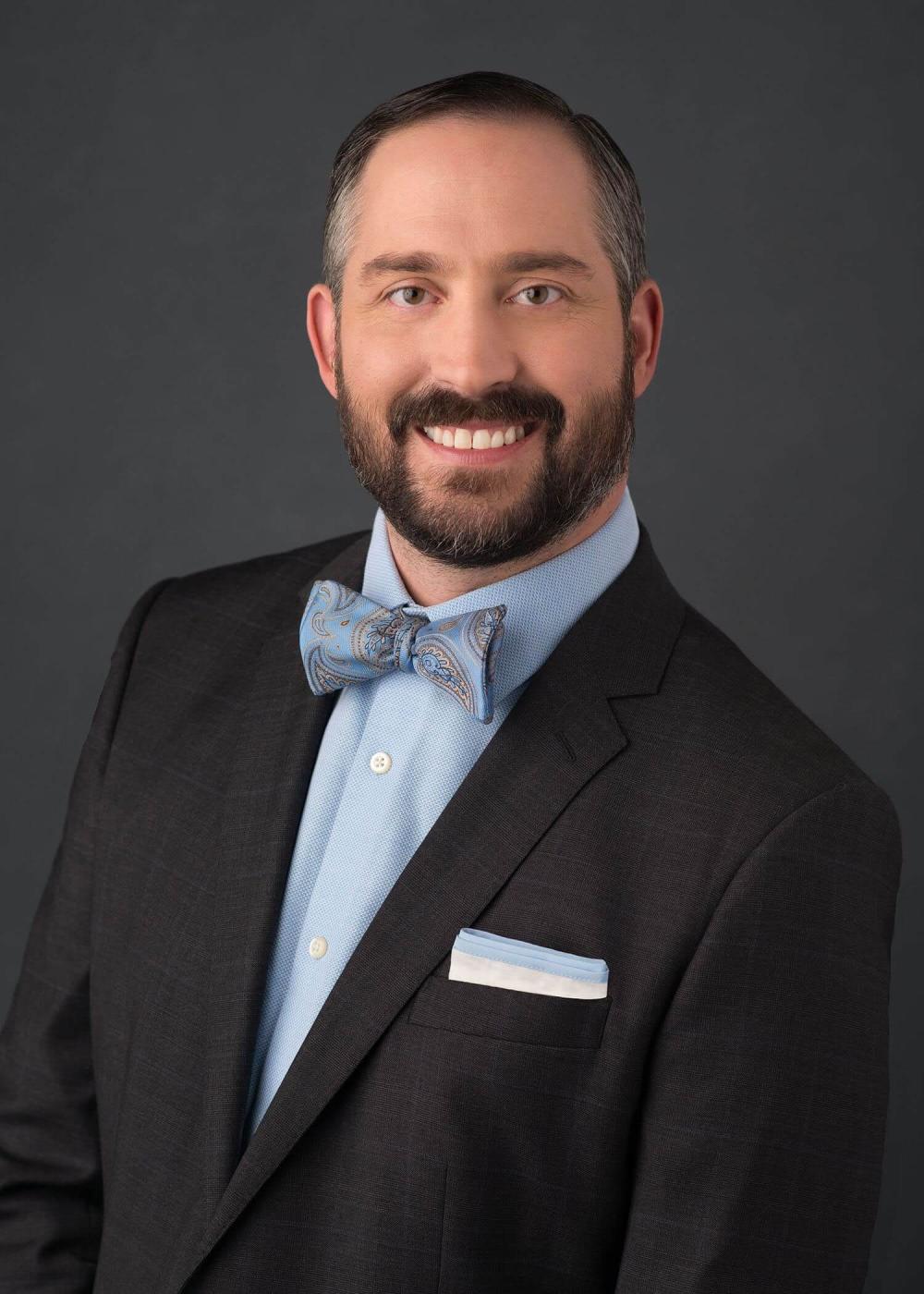 Photo of Matthew “Matt” Laudone in a black suit with a blue dress shirt and blue paisley bowtie
